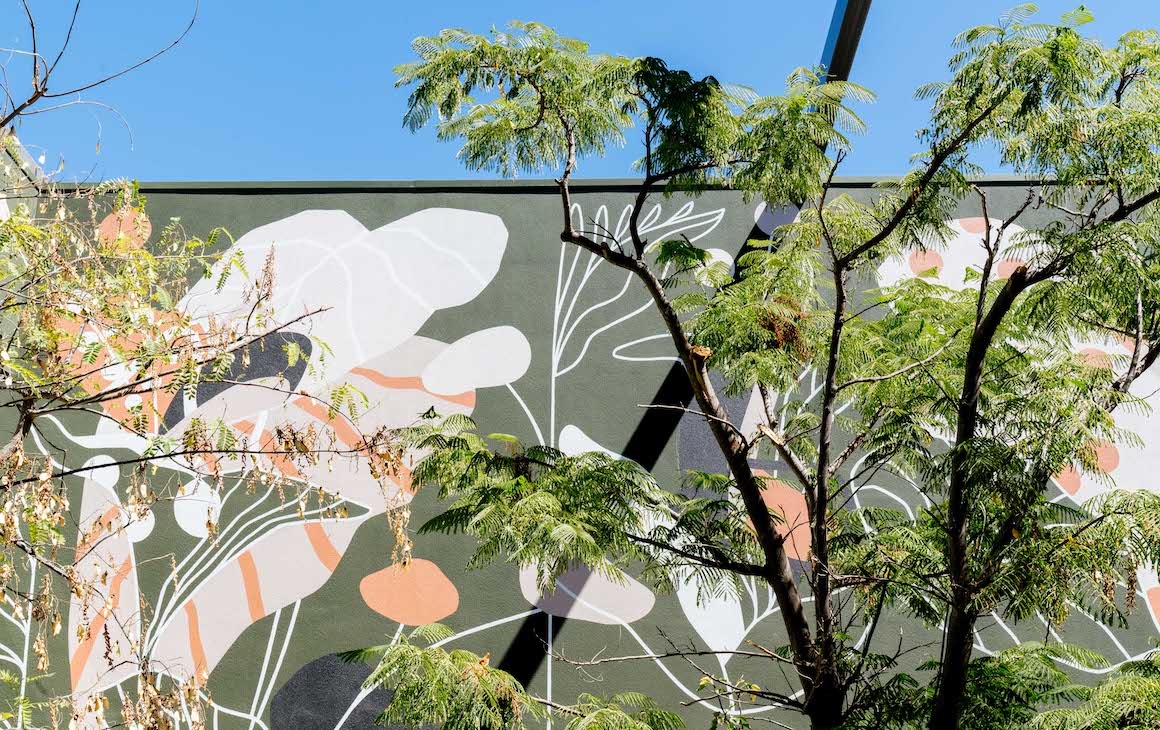 a wall with a mural surrounded by trees and a blue sky