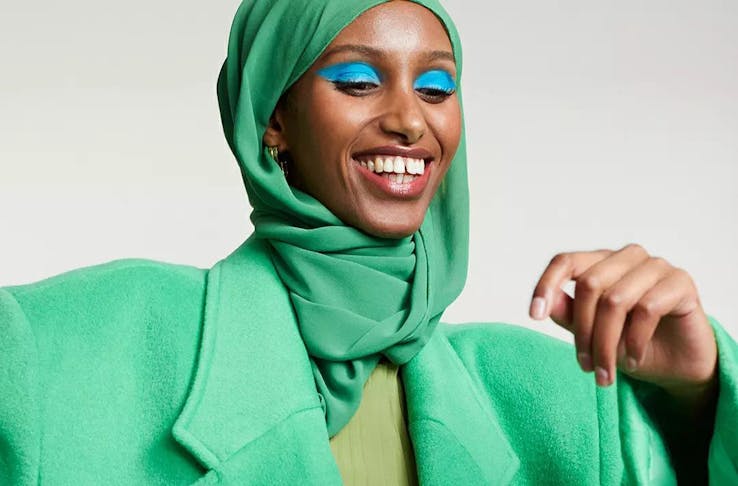 A model wearing a bright green hijab with matching green coat and bright blue eye shadow. 