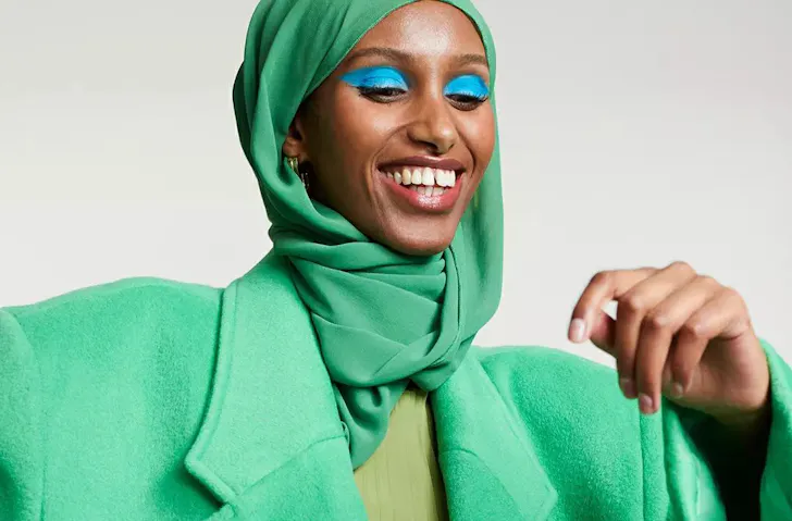 A model wearing a bright green hijab with matching green coat and bright blue eye shadow. 