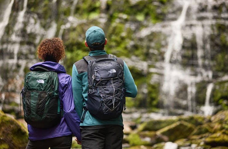 A couple in front of a waterfall with Th North Face backpacks