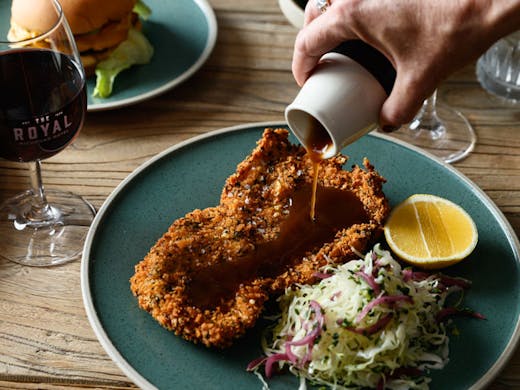 Sauce being poured over a schnitzel. 