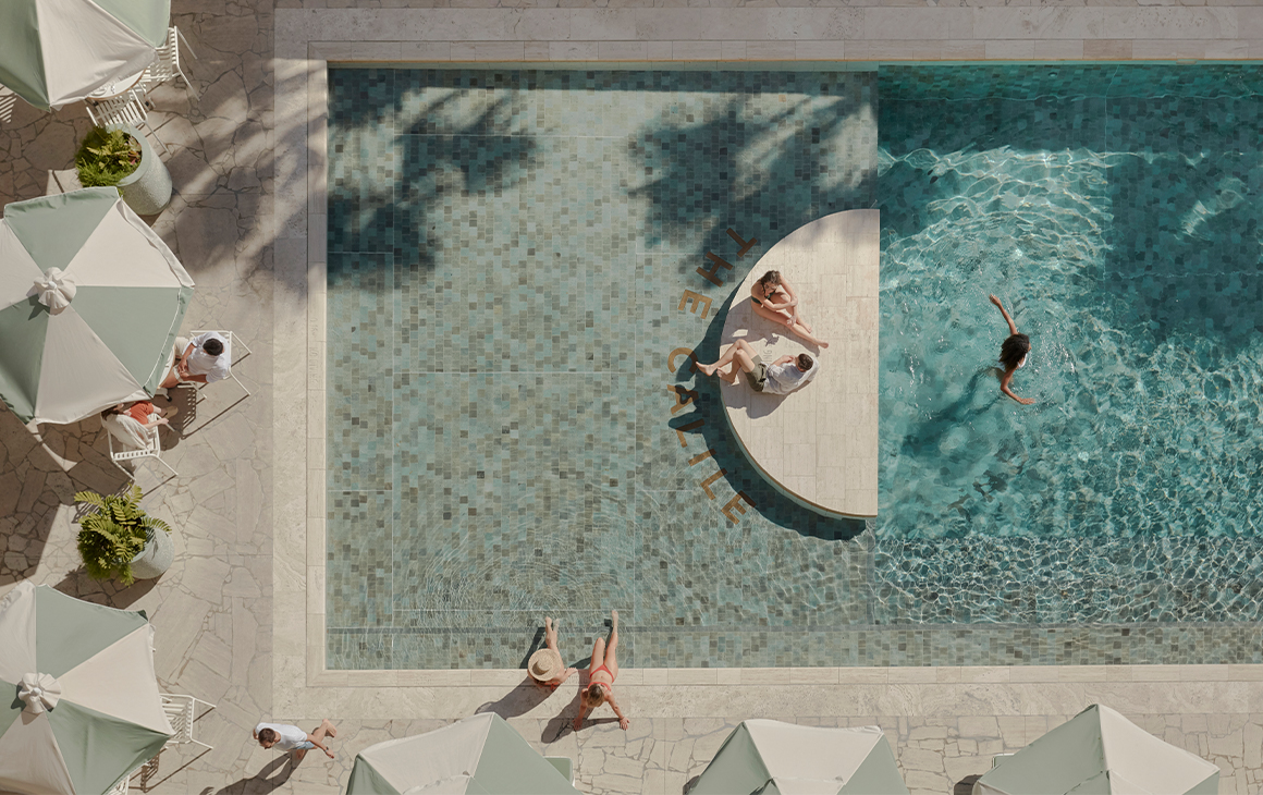 a top down view of a pool with a half moon concrete platform in the middle, and green striped umbrellas around