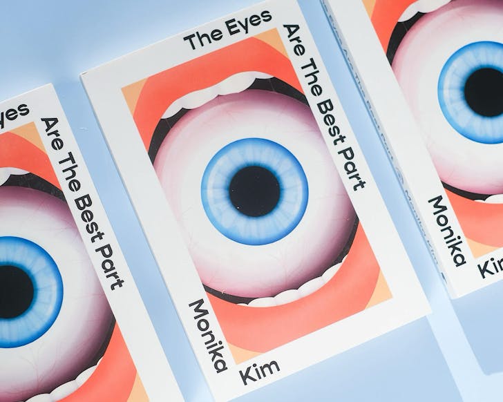 Three books titled 'the eyes are the best part' by 'monika kim' depicting a mouth wrapped around an eyeball with a blue iris. 