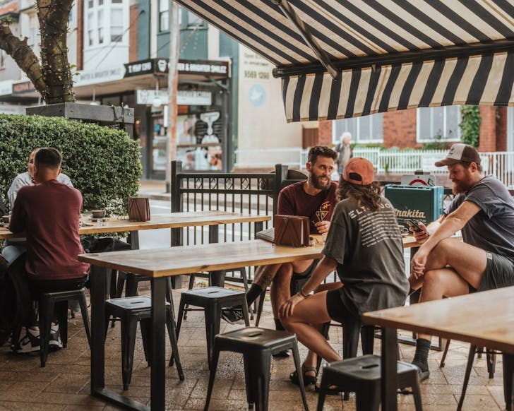 A wide shot of the outdoor front seating of The General Eatery And Supplies, featuring a rustic decor look and people sitting down at the tables chatting.