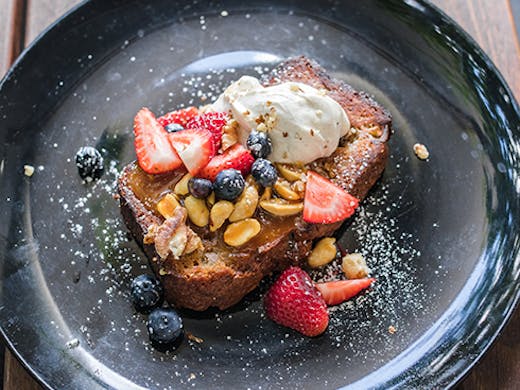 a plate of banana bread topped with fruit and nuts