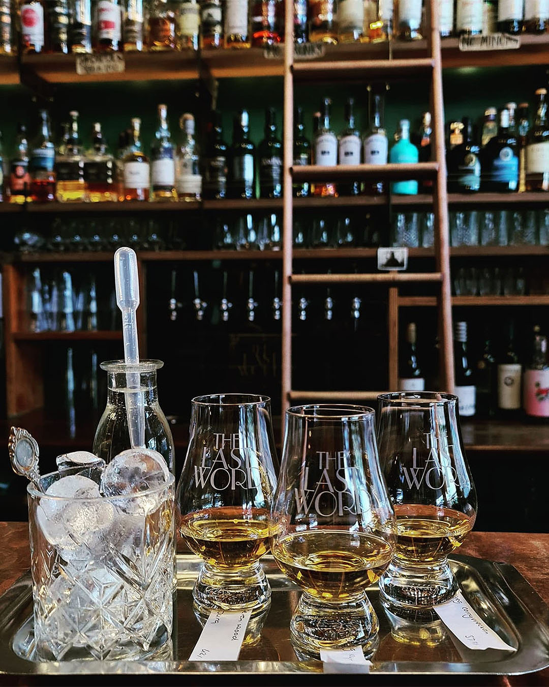 Whiskys sit on a tray in front of a well stocked bar at The Last Word.