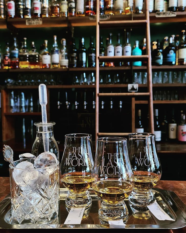 Whiskys sit on a tray in front of a well stocked bar at The Last Word.