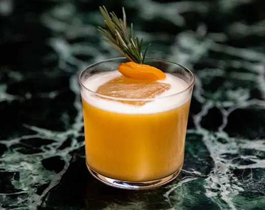 a cocktail with an apricot and rosemary on top