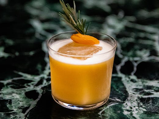a cocktail with an apricot and rosemary on top