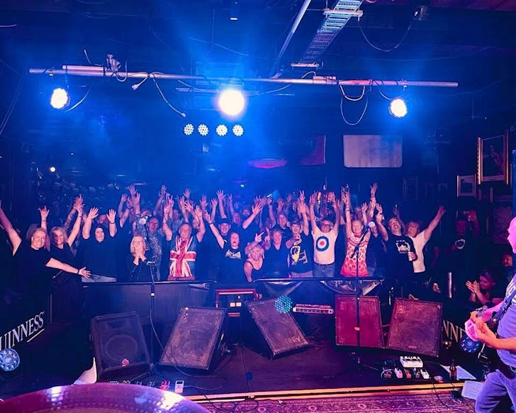 An ecstatic crowd in purple lighting cheers for The Underground on stage.