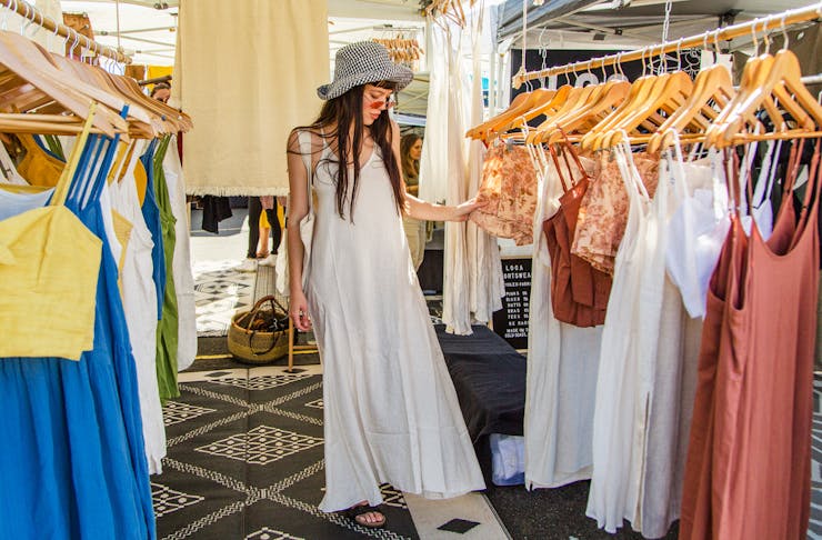 A woman dressed in a white maxi dress looks at racks of clothing at The Village Markets on the Gold Coast.