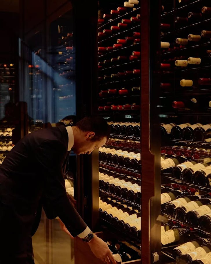 A sommelier grabs a bottle of wine from a tall rack