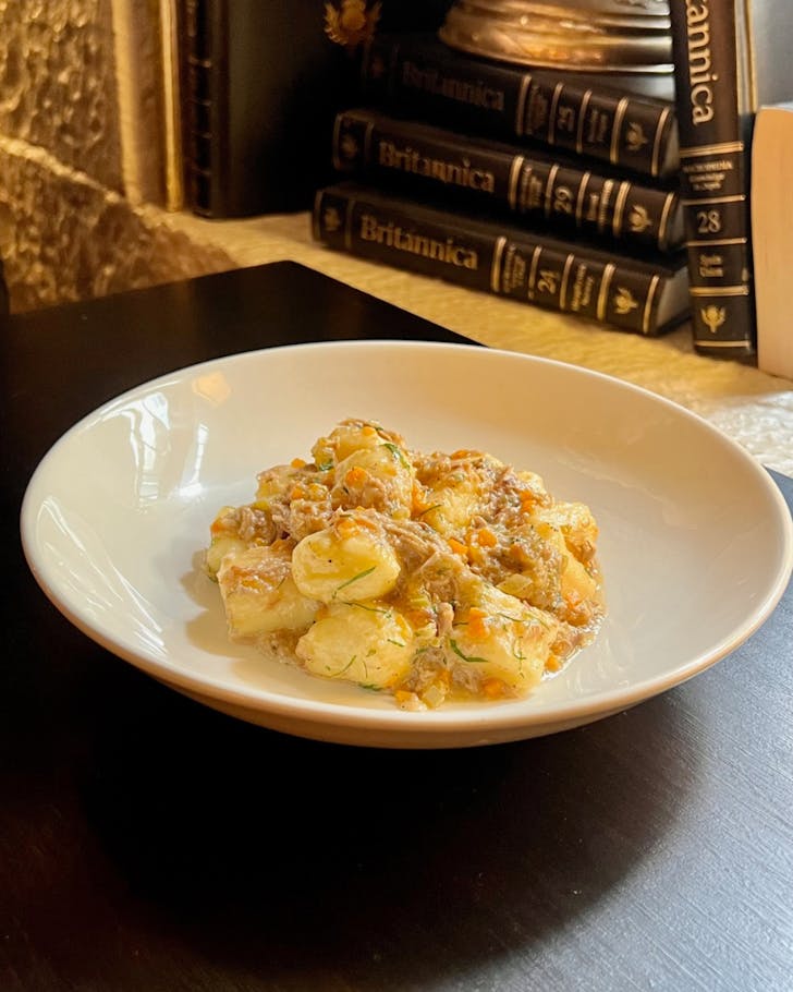 A bowl of pasta on a dark wood tabletop with encyclopedia's in the background