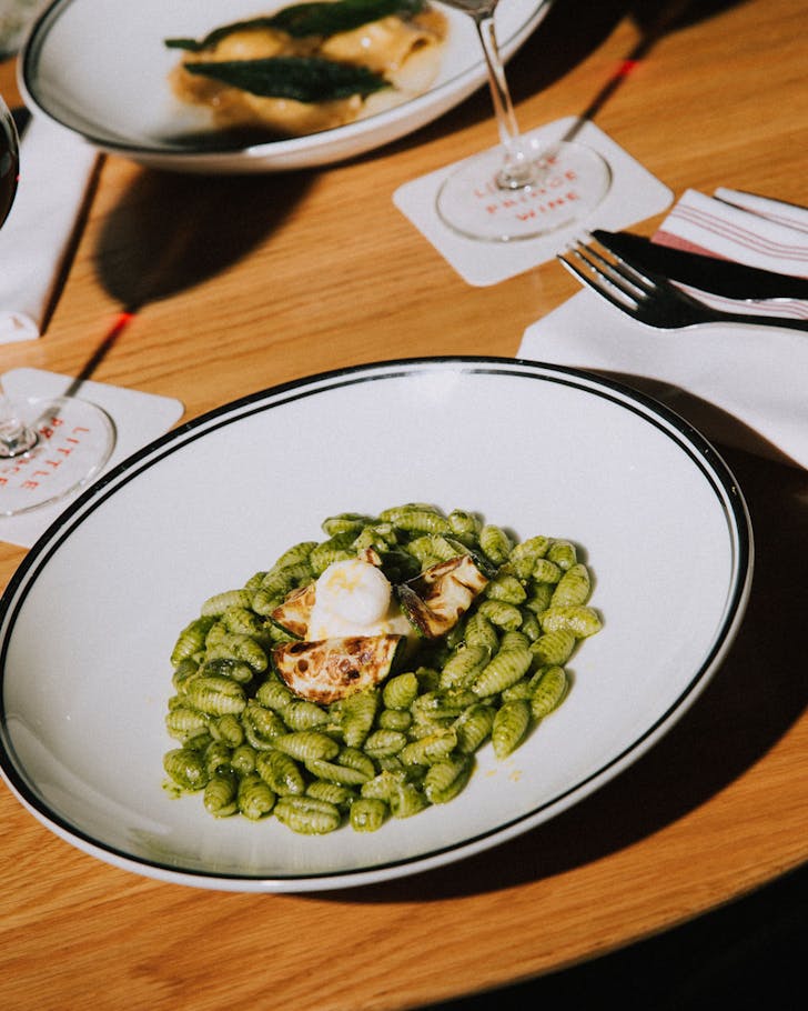 a bowl of pesto pasta on a wooden table