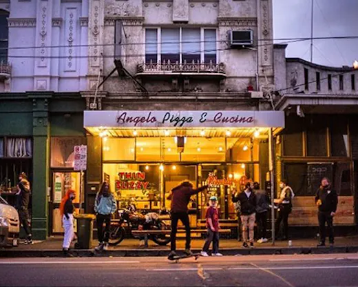 A pizza shop lit up at night with a sign on the window reading 