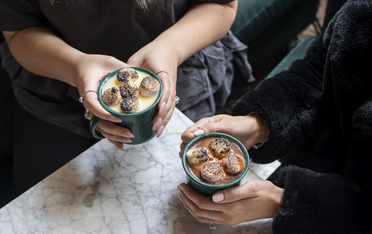 two people holding mugs of hot chocolate