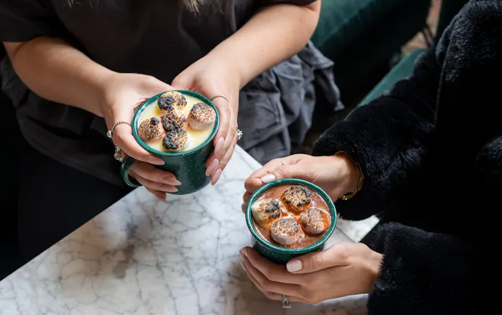 two people holding mugs of hot chocolate