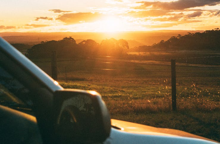 A car is pulled over to watch the sun set over farmland.