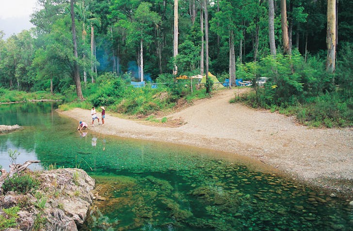Three campers gather by a creek between their campsites and the water.