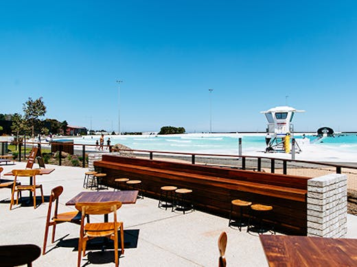 A restaurant next to a large surf park on a sunny day.