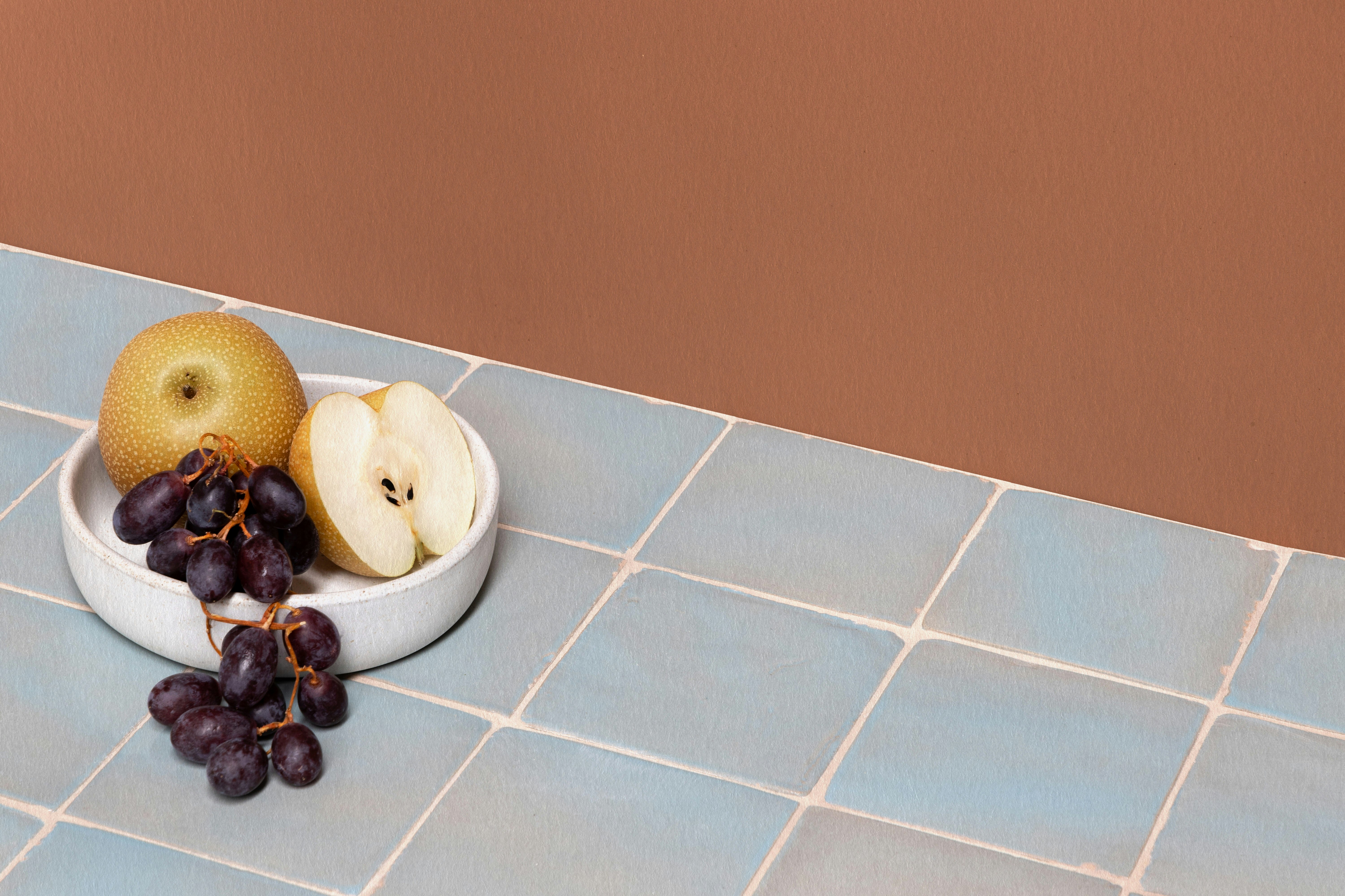 A pretty egg shell blue tiled bench topped with a bowl of fruit. 