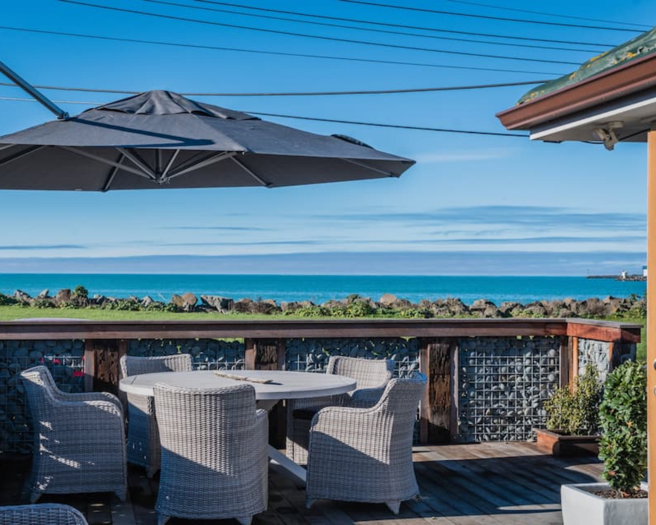 Bright blue ocean and sky are the view from the outdoor dining space at this beach bungalow in Timaru