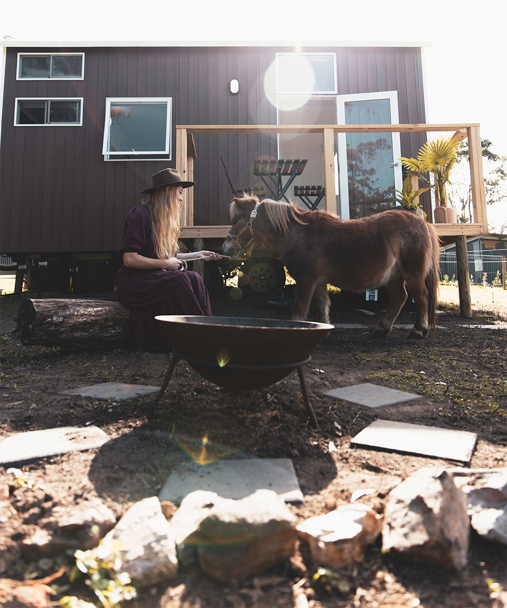 exterior of a black tiny house with a woman patting a shetland pony