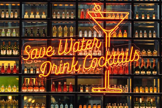 A wall of bottle cocktails with a neon sign