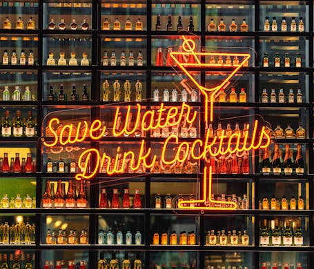 A wall of bottle cocktails with a neon sign