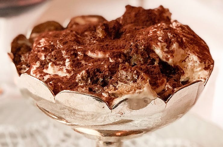 An extreme close up of a delicious tiramisu sitting in a silver bowl dusted with chocolate and just waiting to be devoured.