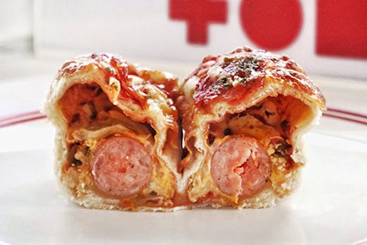 A loaf of pizza bread cut in half to reveal cheese, jalapeños, cheese and a whole sausage.