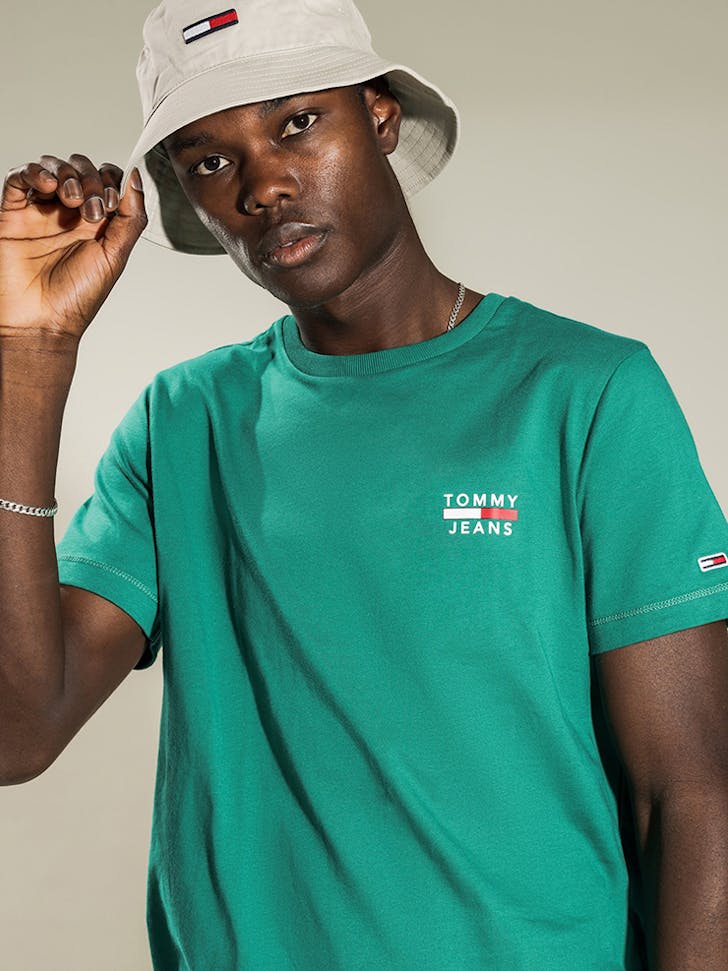 A man wearing a green t-shirt with a Tommy Jeans logo on the right side of the chest.