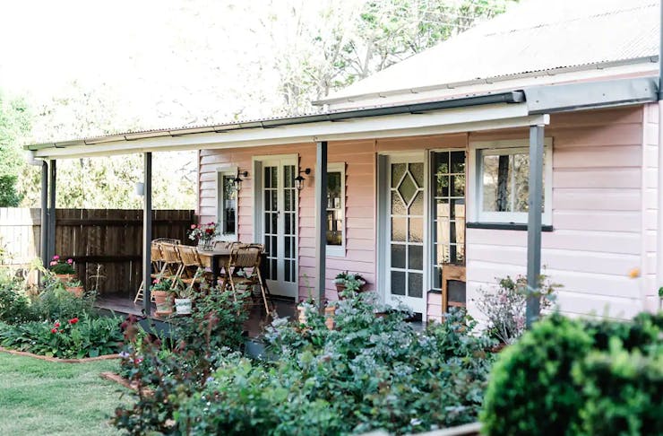 A pink cottage wth a garden and verandah