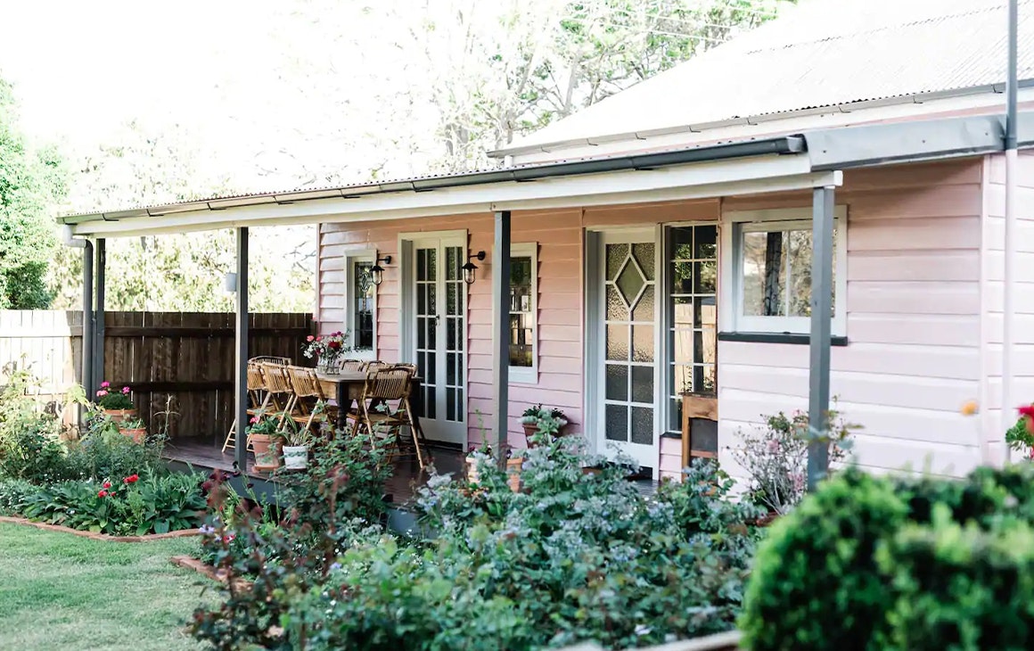 A pink cottage wth a garden and verandah