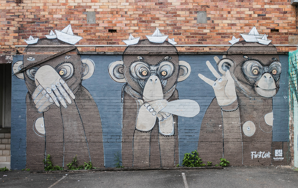 A wall painted with three monkeys in an alleyway