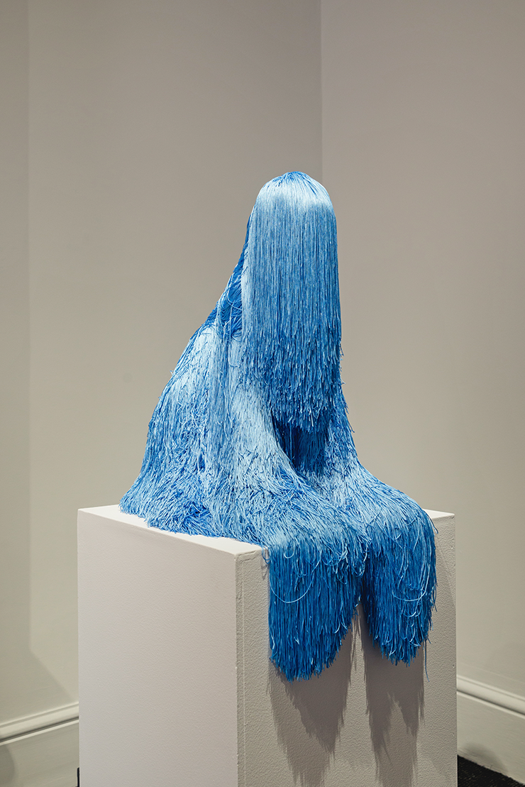 A sculpture of a person sitting on a cube covered in blue tinsel.