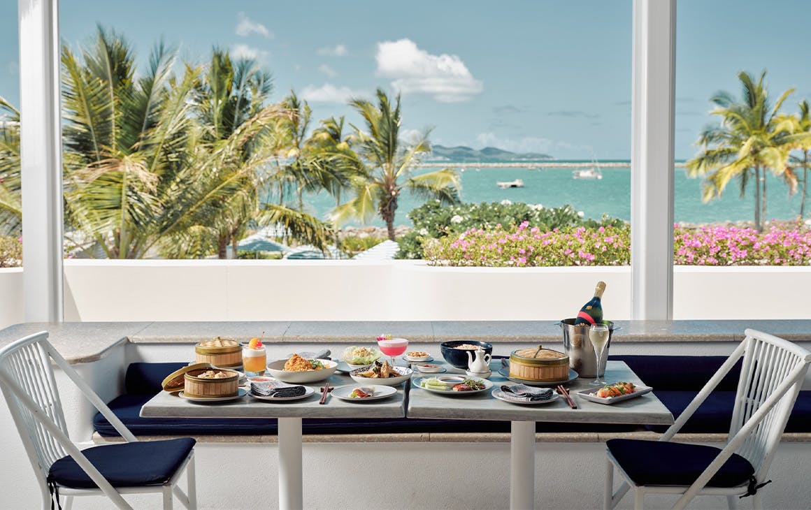 Table covered in plates of food overlooking the ocean and palm trees