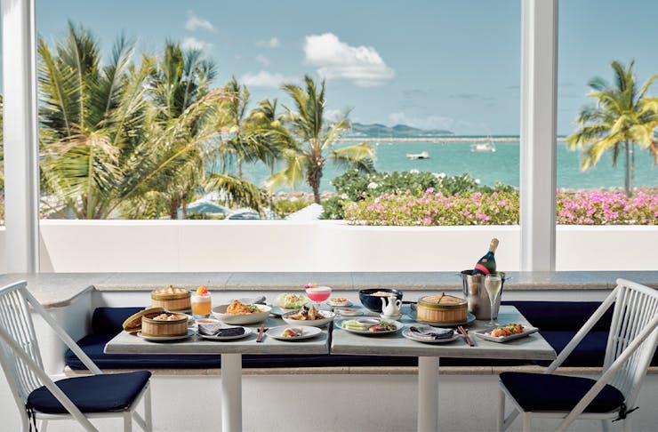 Table covered in plates of food overlooking the ocean and palm trees