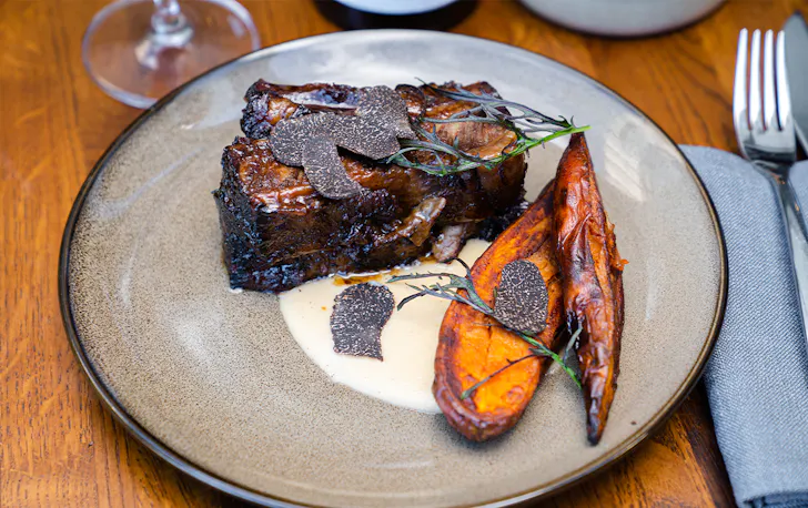 a beef short rib on a plate topped with truffle shavings