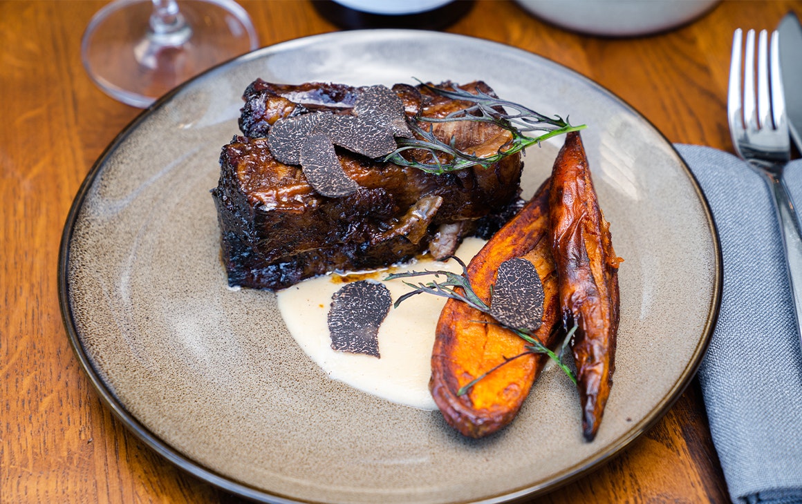 a beef short rib on a plate topped with truffle shavings