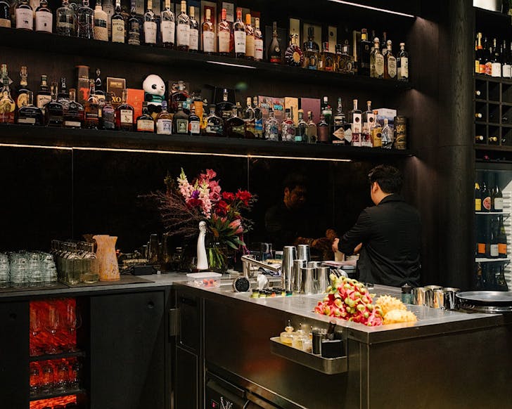 A bartender makes a cocktail while standing in an open-style kitchen.