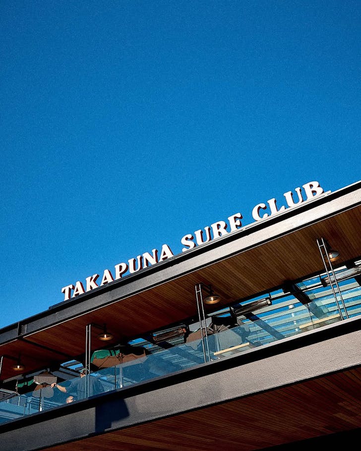A deep blue sky above Takapuna Surf Club, the venue's lettering contrasted against it.