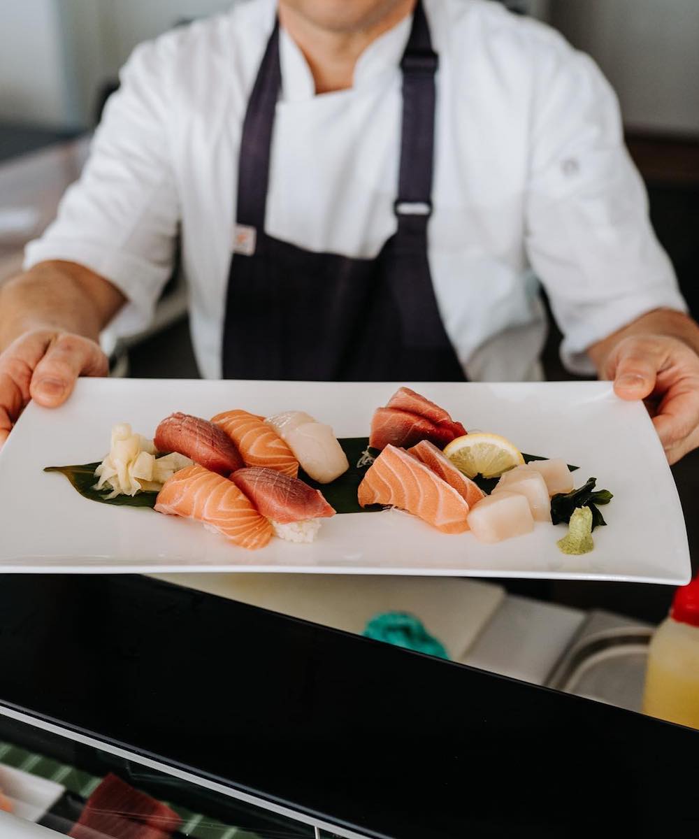 A chef holds a plate of nigiri