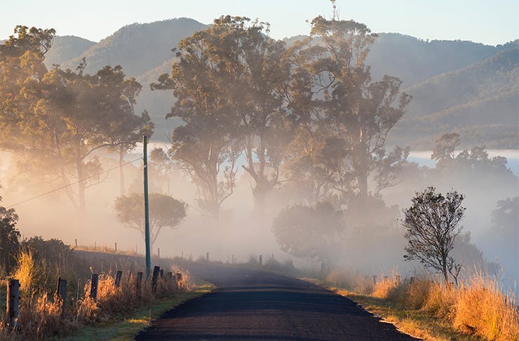 A landscape shot of an empty road leading to a foggy valley. 