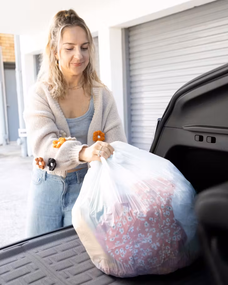 Someone puts a bag of clothing, to be donated, in the back of a car.
