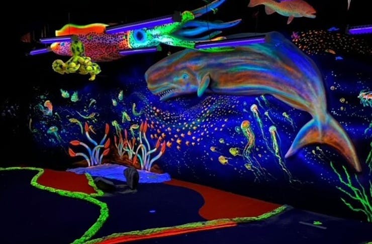 a black lit indoor putt putt course with a whale on the wall