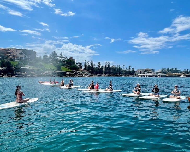 a line up of paddleboards on the water with people in a yoga position