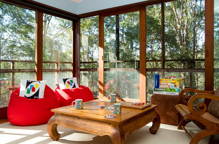 two red bean bags with uno cushions in front of floor to ceiling windows with rainforest views