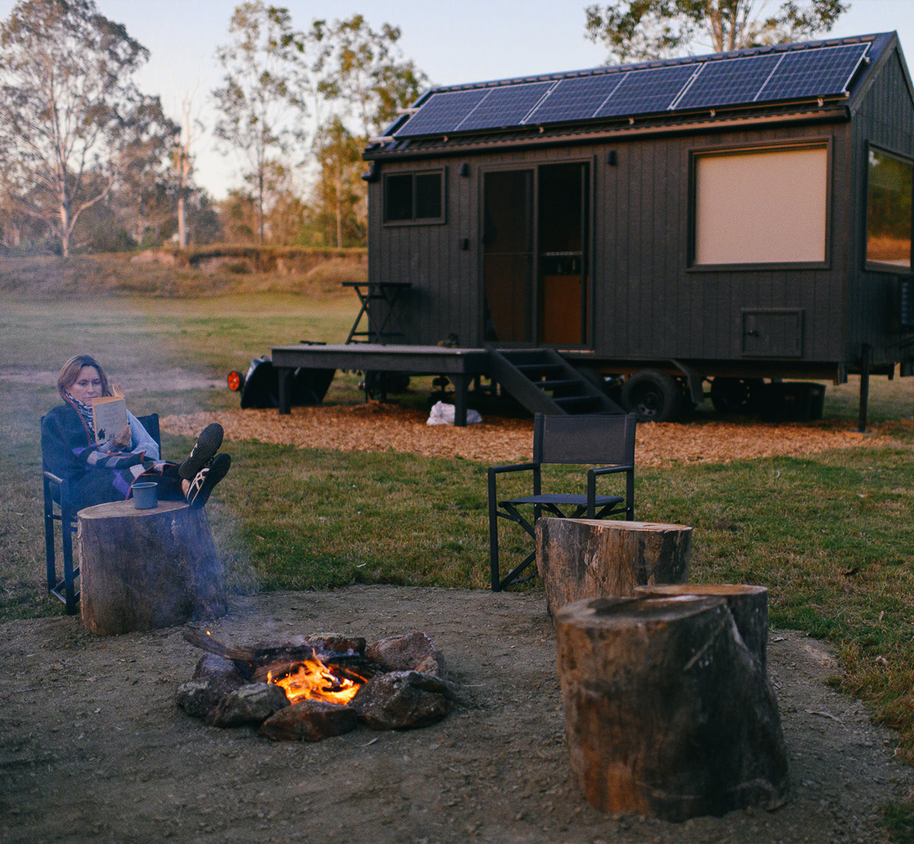 a woman by a campfire in front of a tiny house