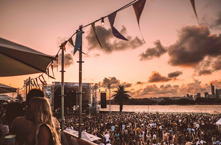 Hundreds of people partying by the water's edge on a balmy, sunlit afternoon.